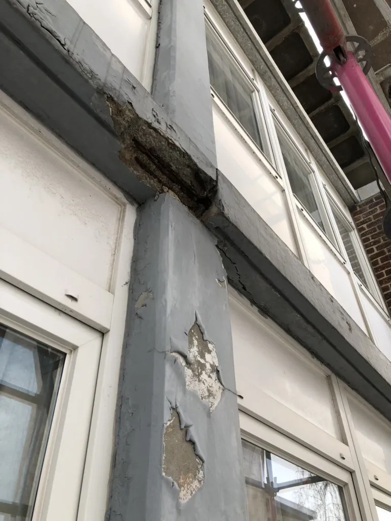 Un montant et une traverse en béton autour d'une baie, revêtement décollé et pertes de matière, échafaudage à côté