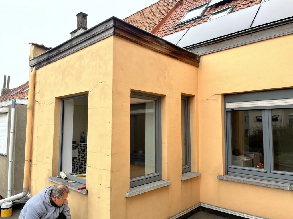 L'annexe avant ravalement, ancien enduit jaune fissuré autour des fenêtres, un intervenant au pied du mur
