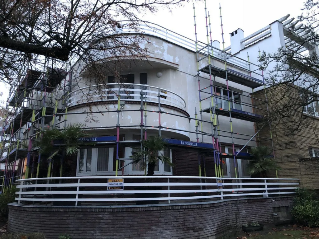 Avant : un bâtiment aux balcons arrondis au début des travaux, échafaudage contre les façades, enduit dégradé