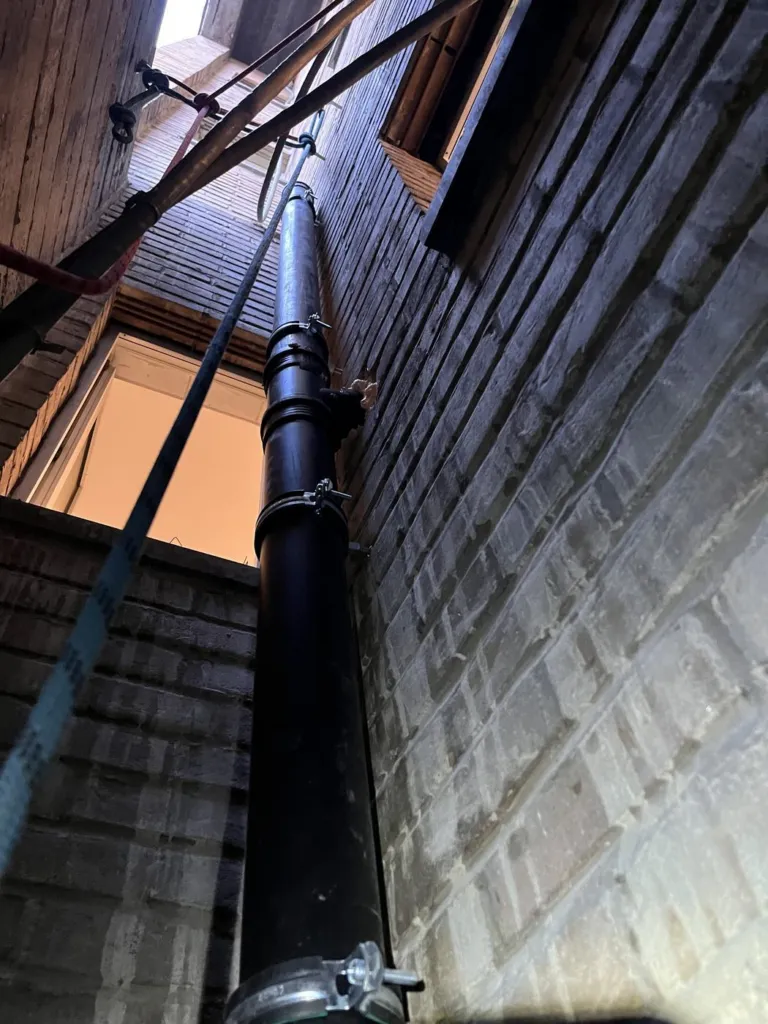 Une canalisation noire fixée par colliers dans un puits étroit entre deux murs de brique