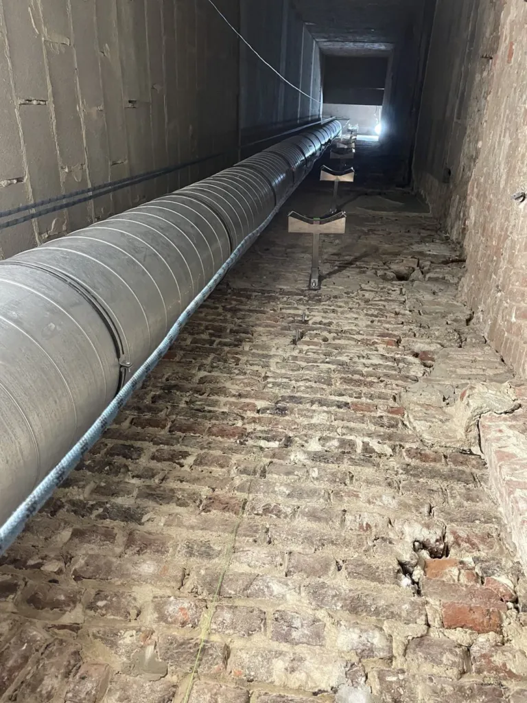 Le conduit métallique spiralé posé le long de la galerie en brique