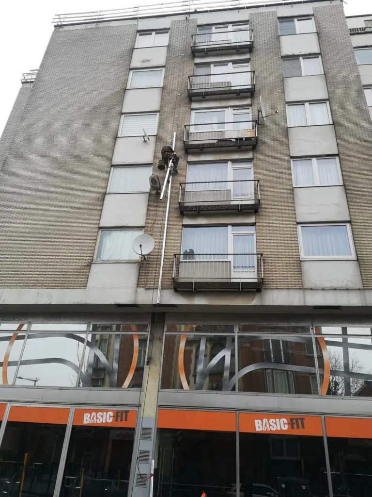 Pendant la pose : un cordiste sur la façade de l'immeuble, la descente déjà partiellement posée le long des balcons