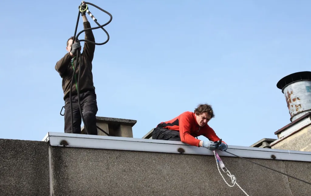 Deux cordistes préparent les cordes en toiture d'une tour de logements, ciel bleu
