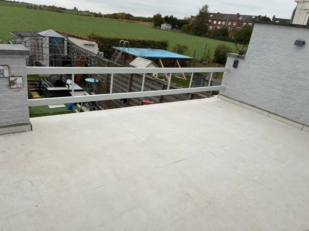 La terrasse carrelée en dalles claires, garde-corps blanc, les champs derrière