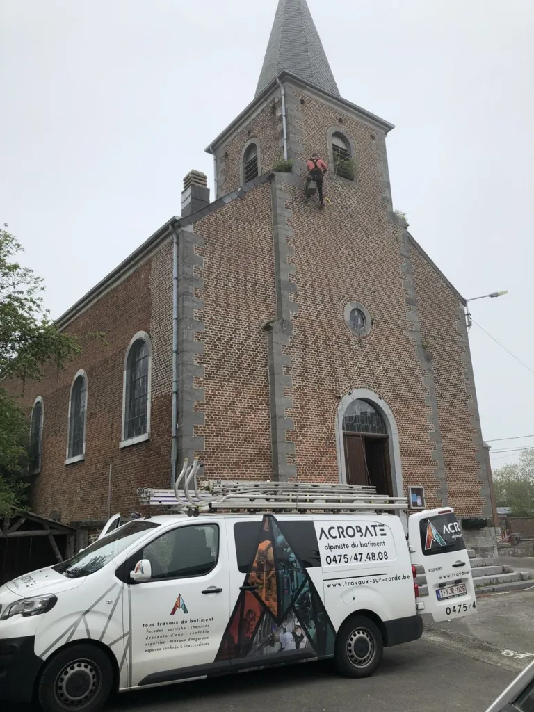 Une église en brique et sa tour à flèche d'ardoise, la camionnette Acrobate garée devant le parvis