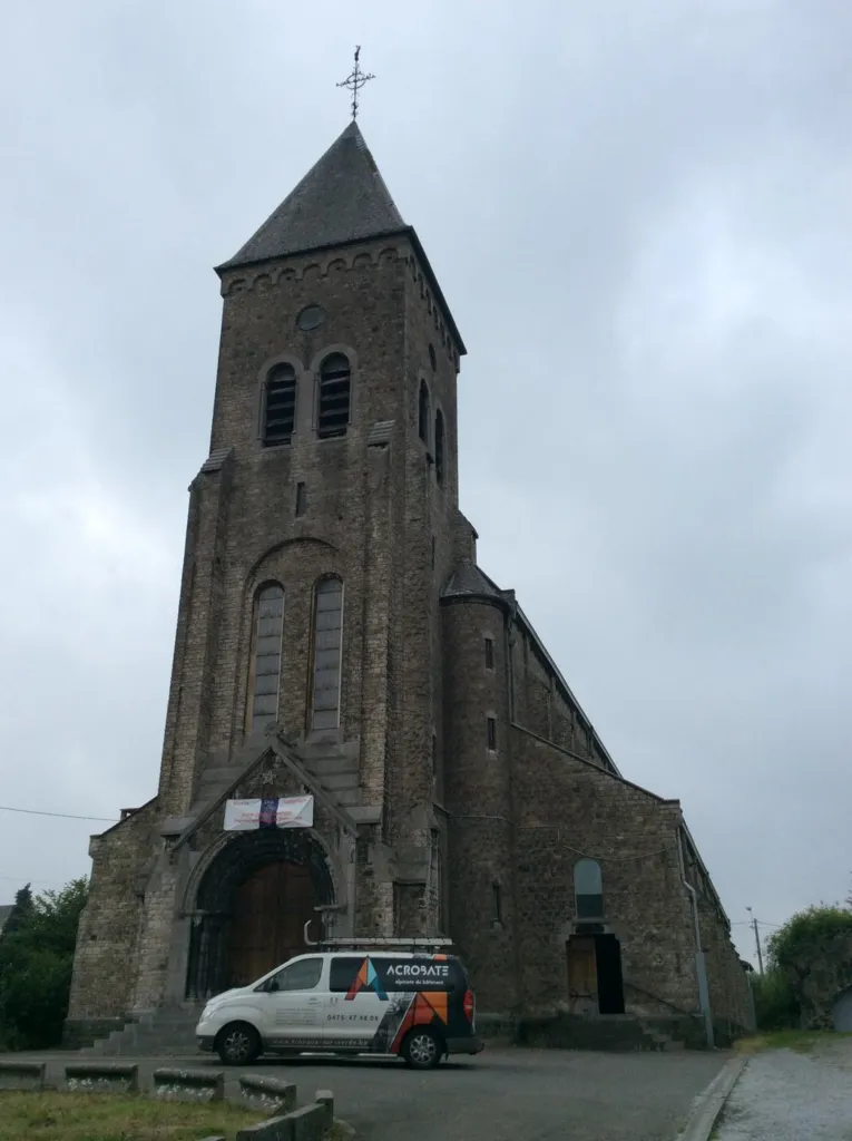 L'église en pierre et sa haute tour, la camionnette Acrobate devant le portail