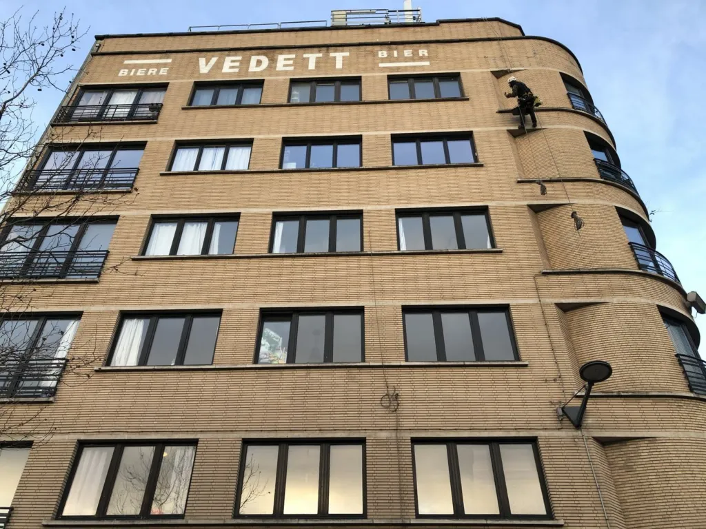 L'immeuble en briques claires vu depuis la rue, un cordiste en façade
