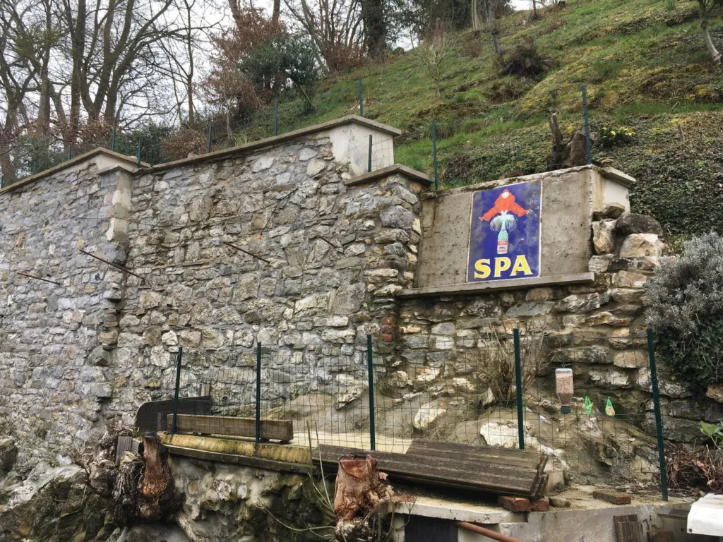 Le même mur après reprise : pierres rejointoyées, couronnements en béton, plaque émaillée conservée