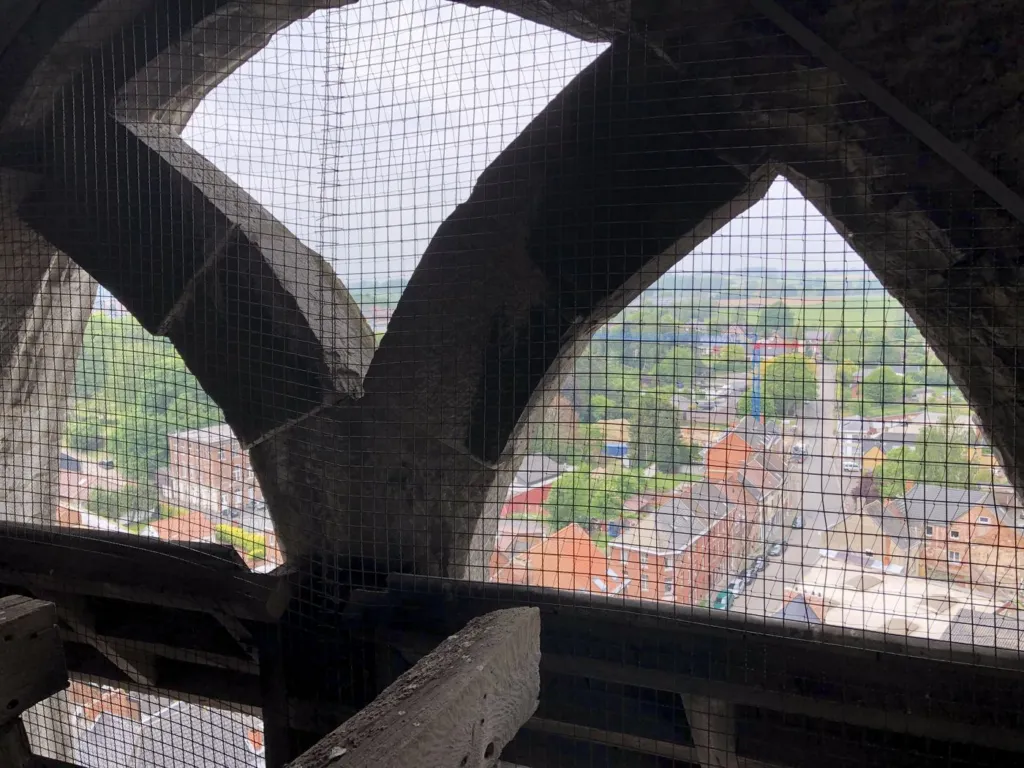 Les baies du clocher vues de l'intérieur, grillage devant les ouvertures, les toits du village en contrebas