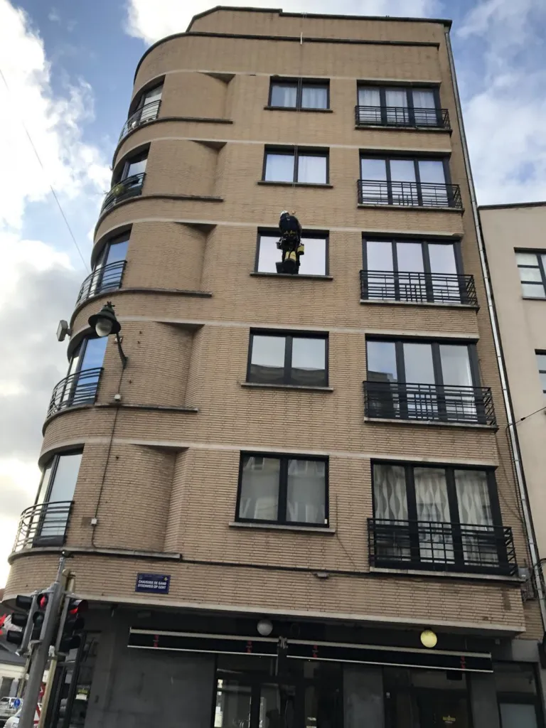 Un immeuble en briques à l'angle arrondi, un cordiste suspendu au niveau d'un bandeau de façade