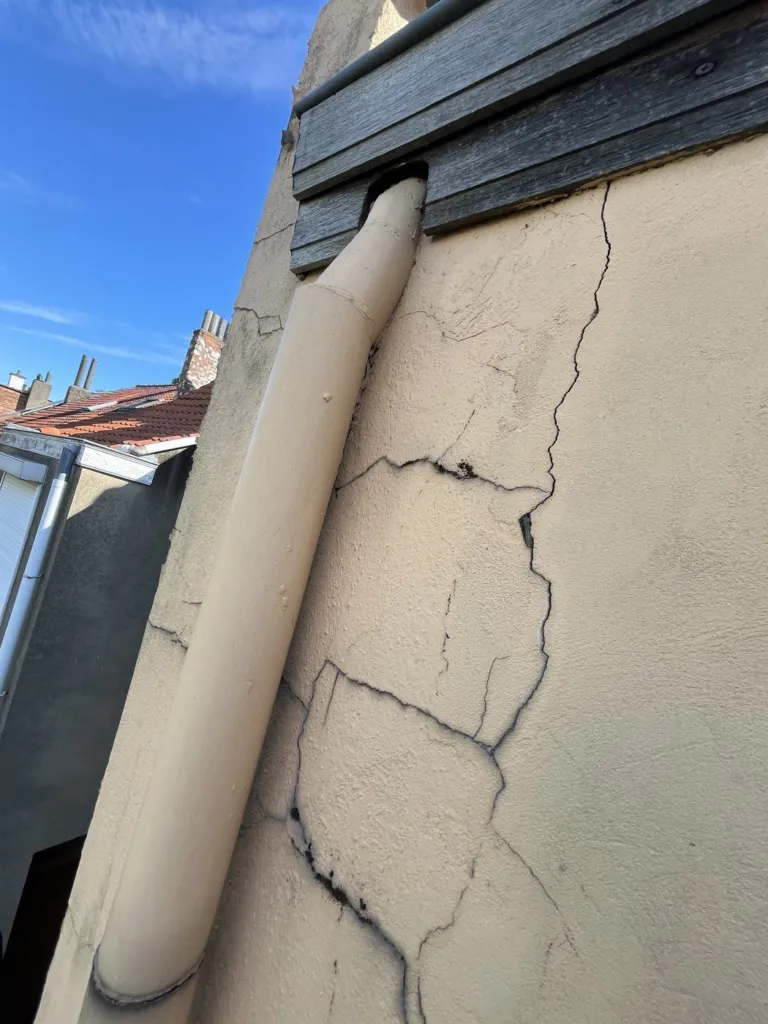 Les fissures de l'ancien enduit près d'une descente d'eau