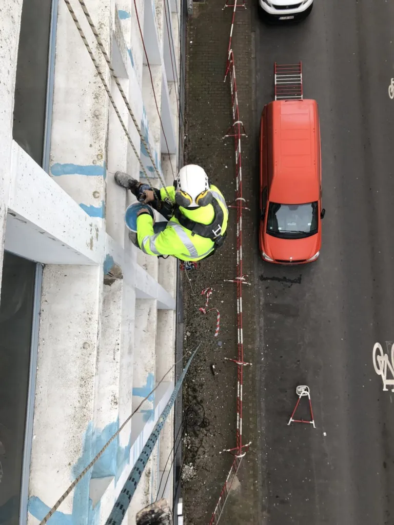 Un cordiste en gilet jaune travaille sur la trame de béton d'un immeuble de bureaux, la rue en contrebas