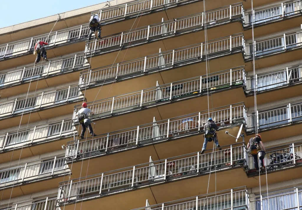 Six cordistes répartis sur plusieurs niveaux de balcons de la tour, chacun sur sa corde