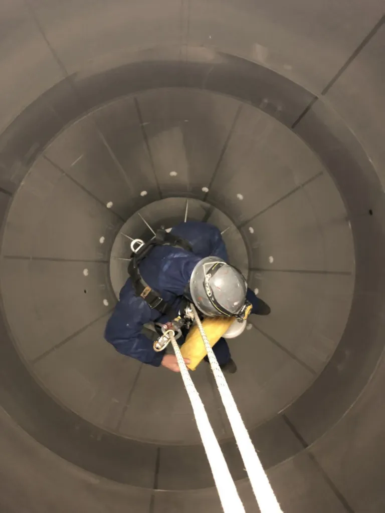 Cordiste en suspension à l'intérieur d'un silo métallique, vu depuis la trappe