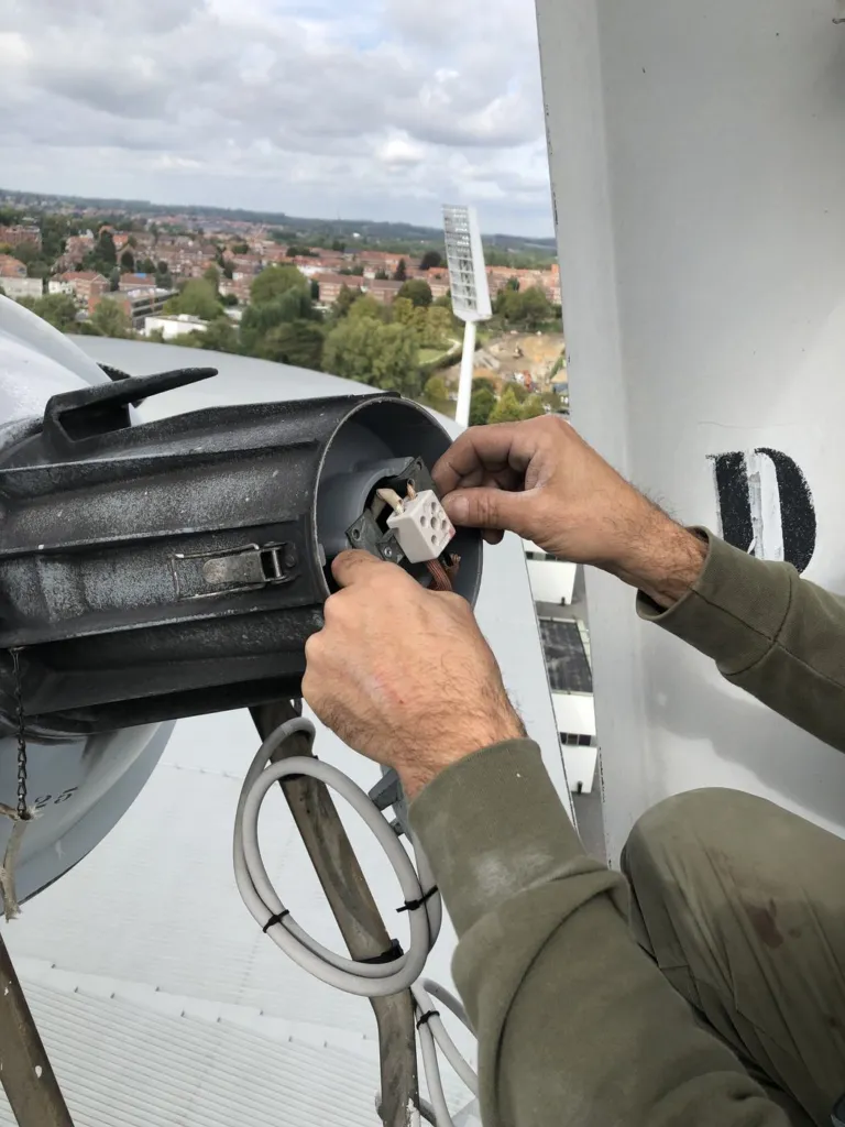 Intervention sur les connexions d'un projecteur ouvert, en tête de mât, la ville en arrière-plan