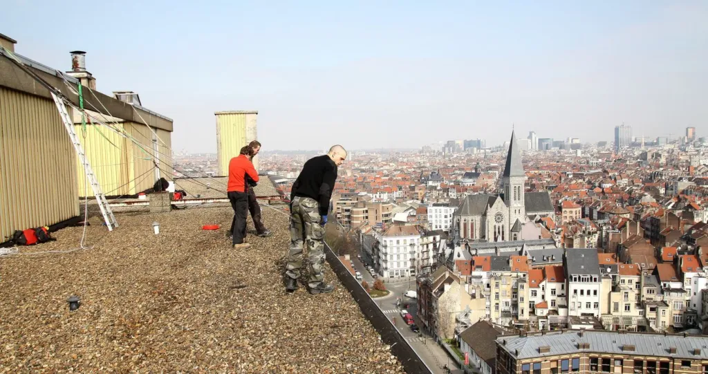 Deux cordistes préparent le matériel sur la toiture-terrasse, Bruxelles en fond