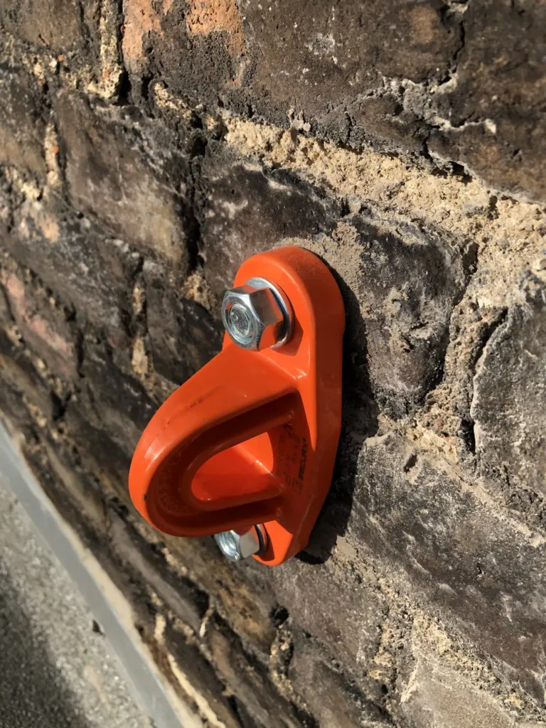 Plaquette d'ancrage orange boulonnée dans un mur de briques