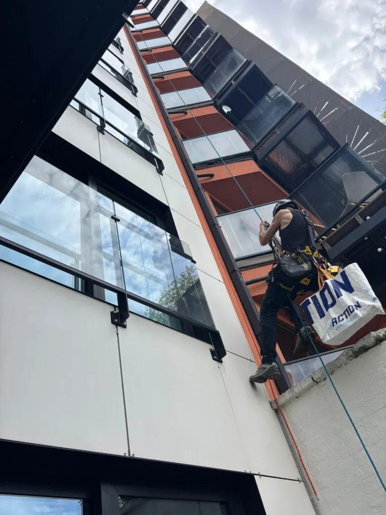 Un cordiste suspendu sous les balcons d'un immeuble récent, au niveau des poutres métalliques