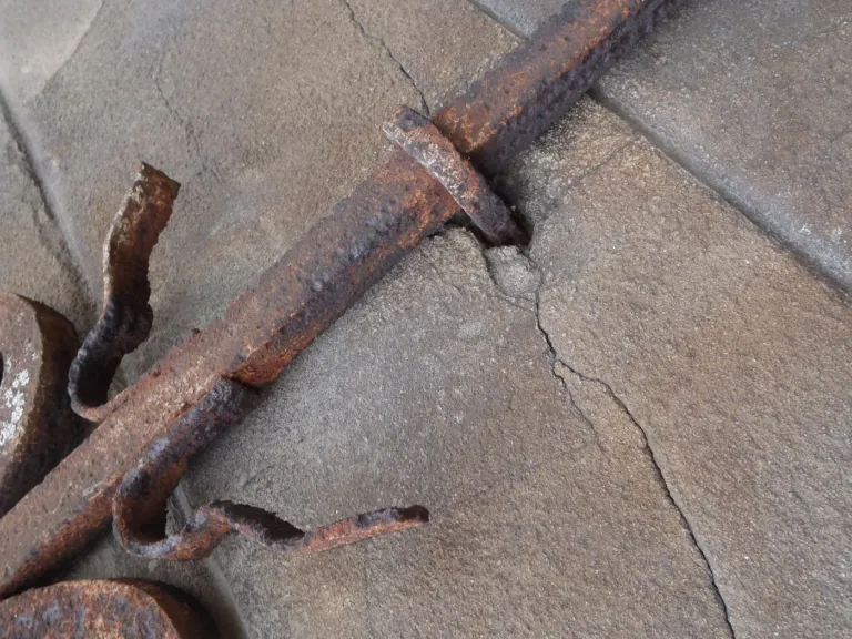 Fissure dans un élément de façade en pierre, au pied d'un fer scellé rouillé, photographiée de près depuis la corde