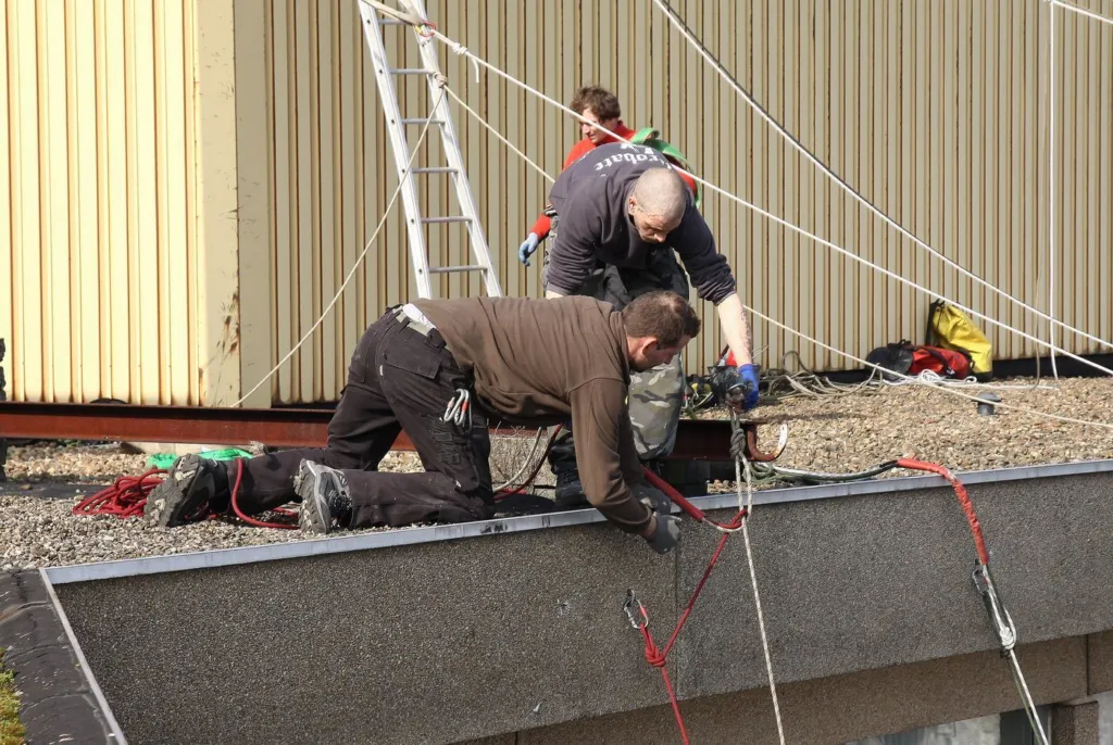 Trois cordistes installent les cordes en rive de toiture, au-dessus des balcons