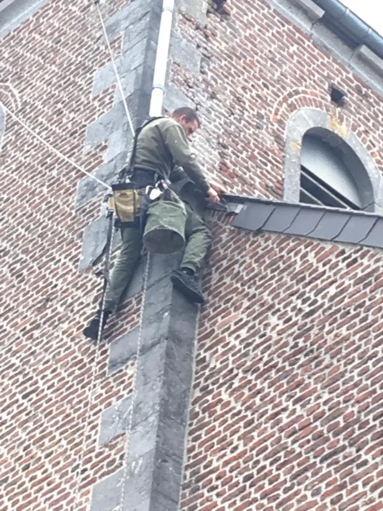 Le cordiste suspendu contre la brique, près d'une baie encadrée de pierre