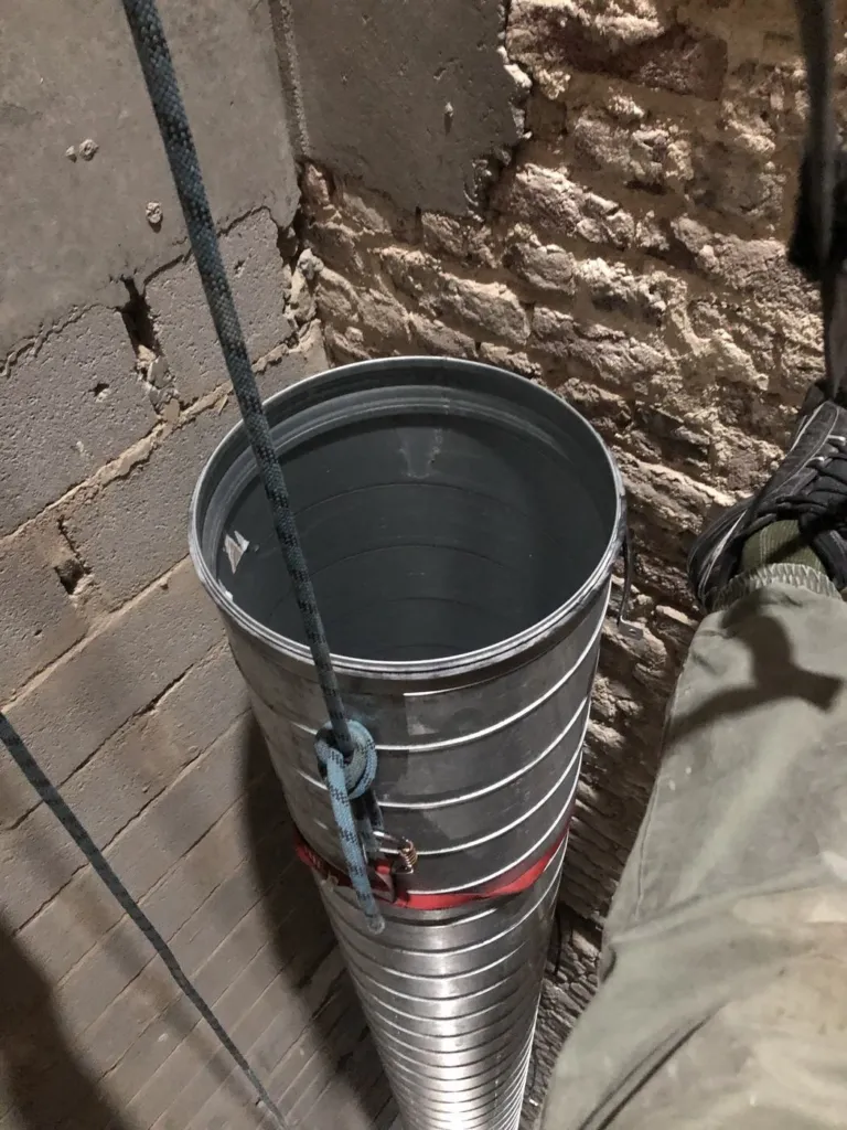 Un tronçon de conduit manœuvré sur cordes dans la gaine