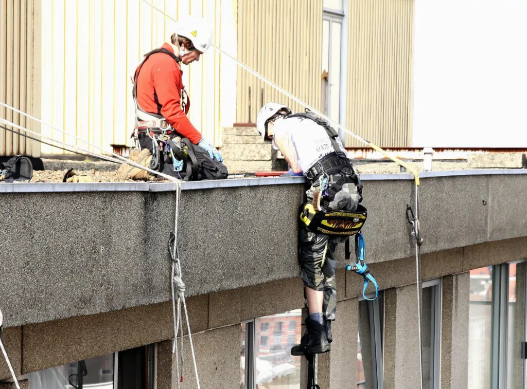 Un cordiste franchit la rive de la toiture pour descendre en façade, un second l'assure