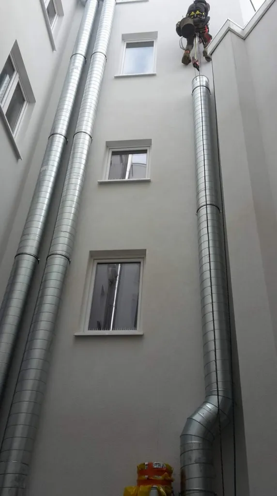 Cordiste posant une section de conduit en façade