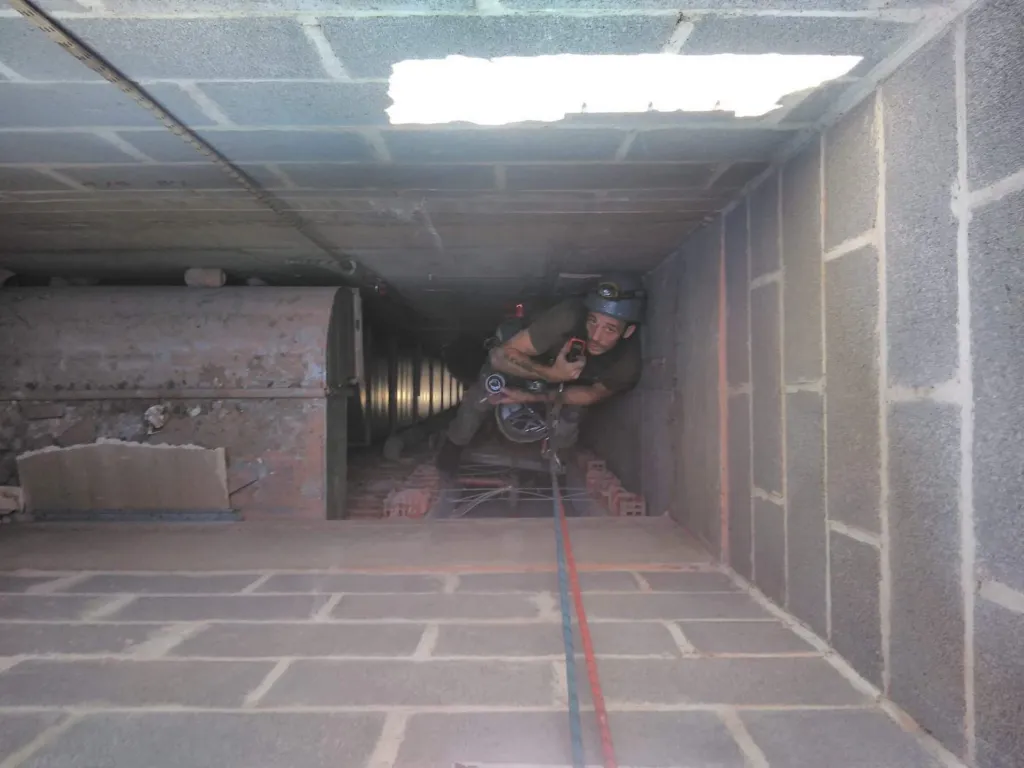 Un cordiste au fond de la gaine en blocs de béton, éclairé par l'ouverture