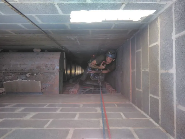 Un cordiste au fond d'une gaine technique en blocs de béton, entre les conduits d'un site industriel