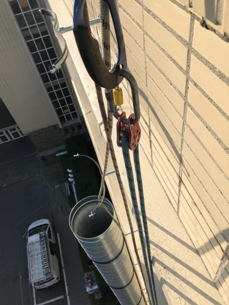 Manutention d'une section de conduit sur corde, le long de la façade
