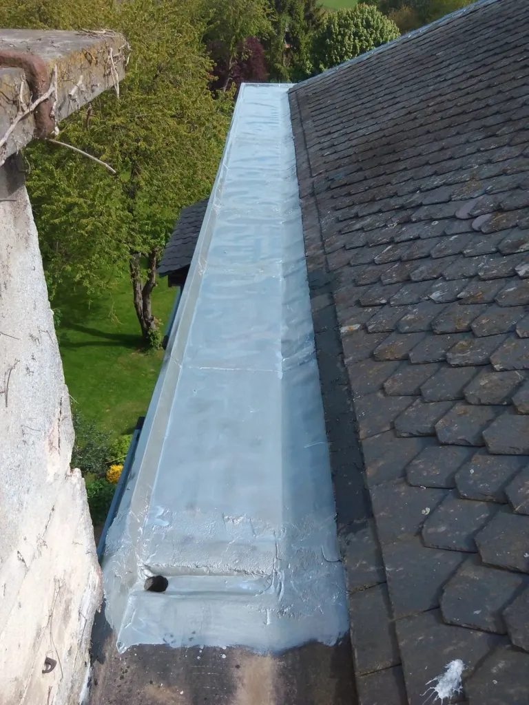 Chéneau en zinc le long d'une toiture en ardoises, vu depuis la corde