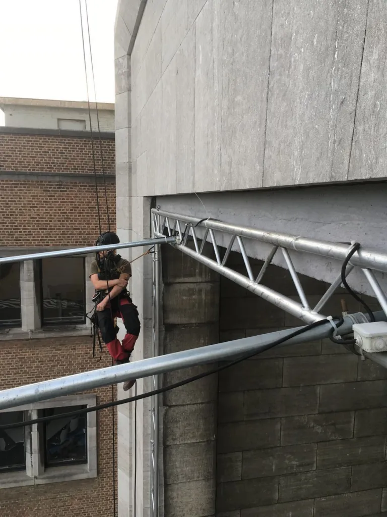 Un cordiste travaille sur la traverse du cadre métallique devant la façade
