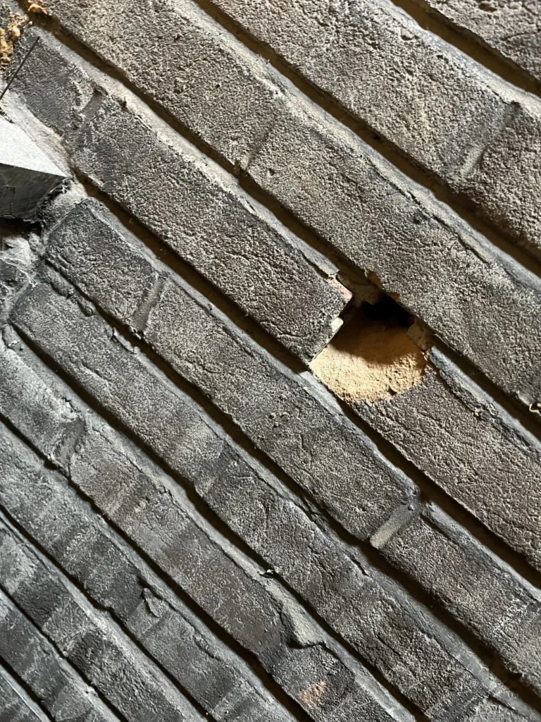 Une ouverture percée dans le mur de brique pour le passage du tube