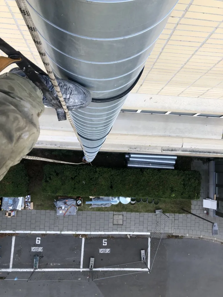 Pose d'un conduit vue en plongée depuis la toiture, le cordiste au contact de la façade