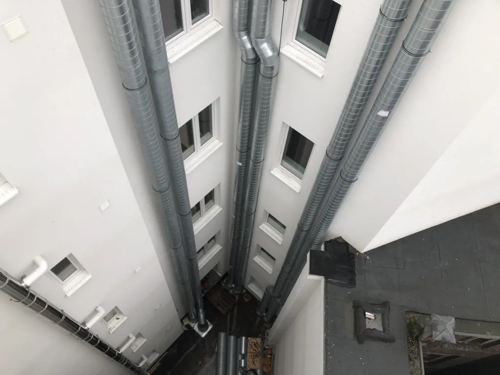 Cour intérieure vue en plongée depuis la toiture, quatre conduits d'aération montant le long des façades, Liège