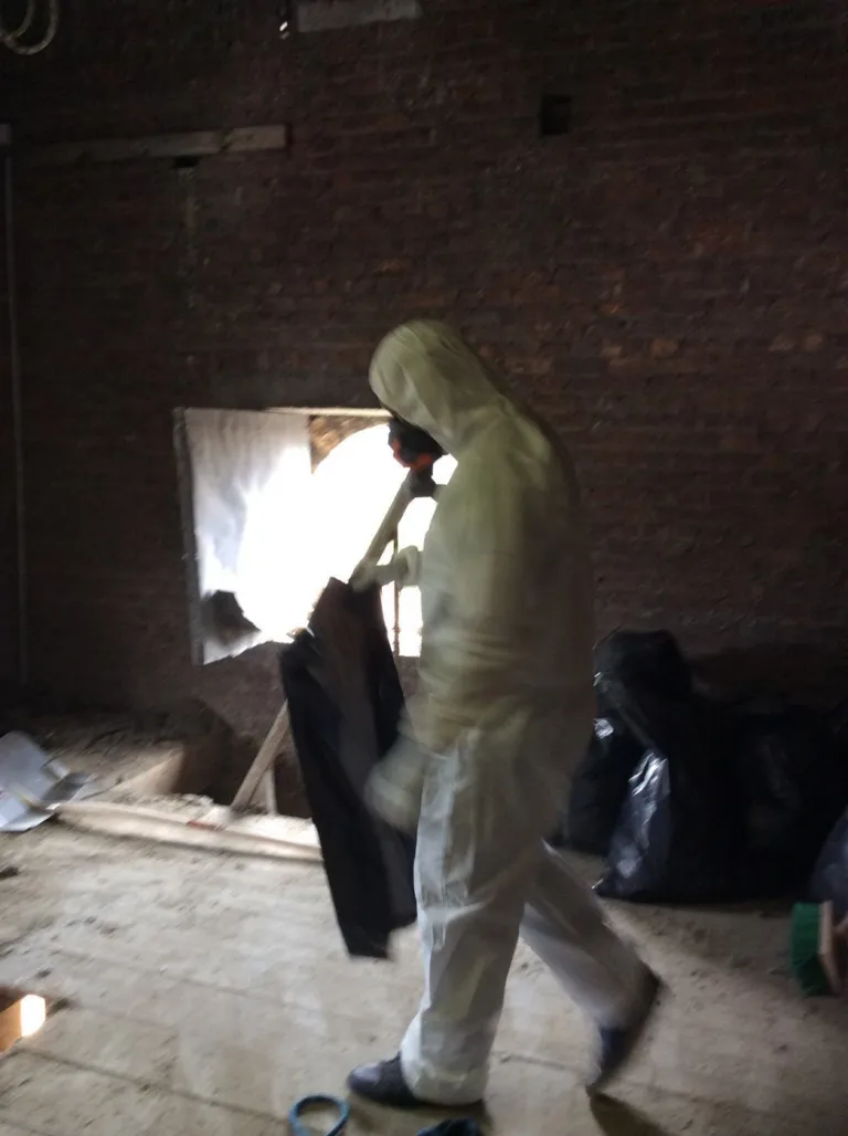 Un intervenant en combinaison et masque ramasse les dépôts de pigeons sur le plancher d'un clocher