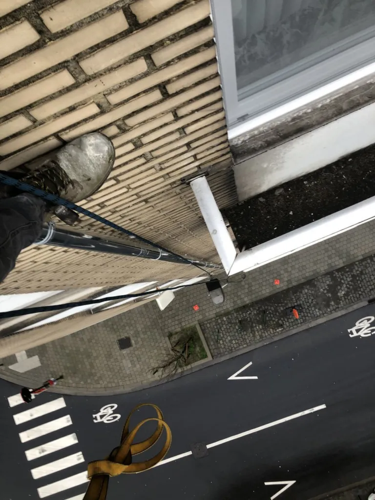 Descente d'eau vue en plongée depuis la corde, le long d'une façade en brique, le trottoir sept niveaux plus bas, Etterbeek