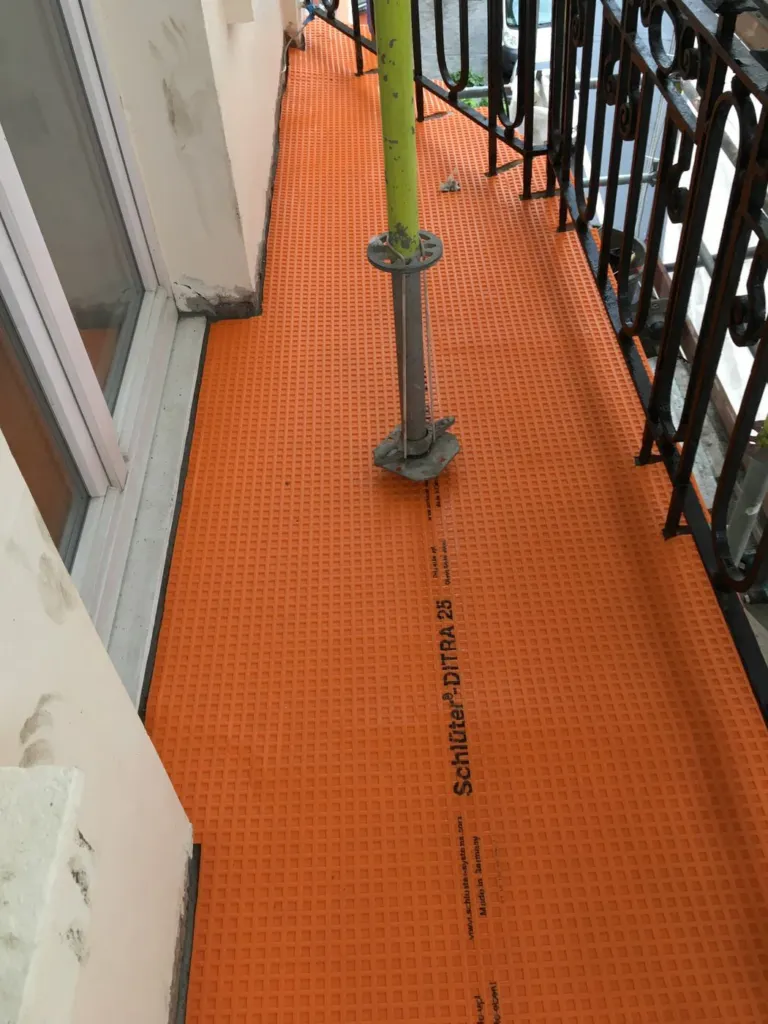 La natte orange posée sur le sol du balcon, sous le futur revêtement
