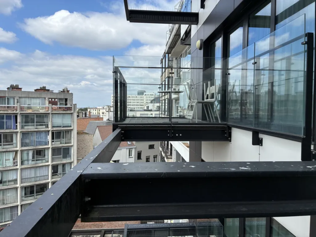 Les poutres métalliques noires qui portent les balcons vitrés d'un étage, nues, vues depuis la terrasse haute